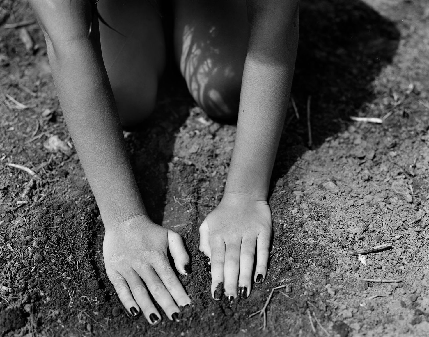 A young person with painted nails pressing their palms into the dirt.